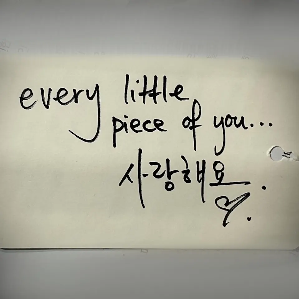 종이 위에 검은 펜 같은 선으로 영문 every little piece of you...와 한글 사랑해요가 적혀 있어요. 하트와 점도 함께 보여요.