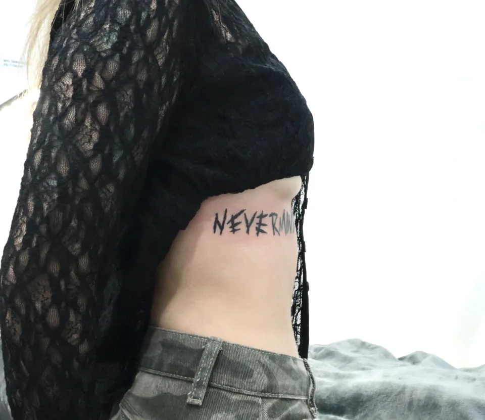 같은 NEVERMIND 작업을 옆에서 본 모습이에요. 글씨가 갈비뼈 쪽 몸 선을 따라 놓여 있고 오른쪽 끝은 옷 가장자리에 가려 있어요.