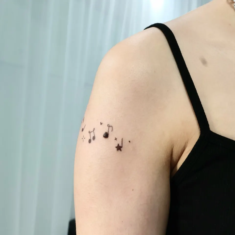 어깨 가까이에서 찍은 근접 사진. 음표 줄의 한쪽 끝이 화면 가장자리로 이어지고 별과 작은 점이 보임.